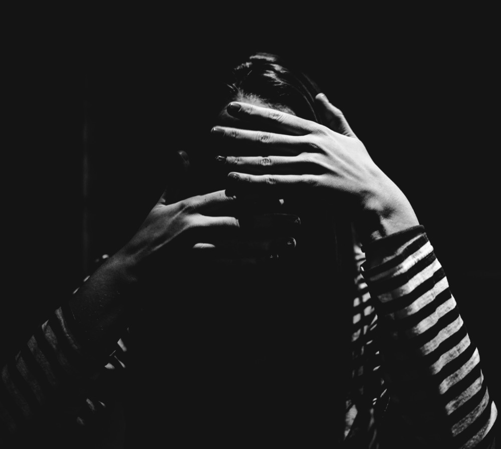 Person experiencing emotional overwhelm and anxiety in dark setting symbolizing trauma, stress, depression, and the importance of compassionate mental health support and therapy